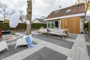 A modern outdoor patio with a wooden deck, white furniture, and potted plants.