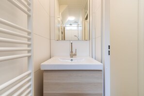 A modern bathroom with a white sink, a mirror, and a shower.