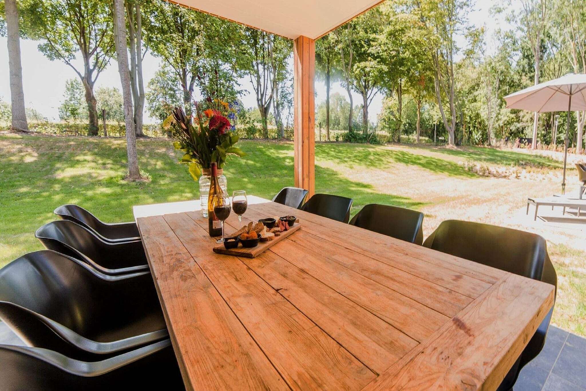 An outdoor dining area with a wooden table, black chairs, and a large umbrella.