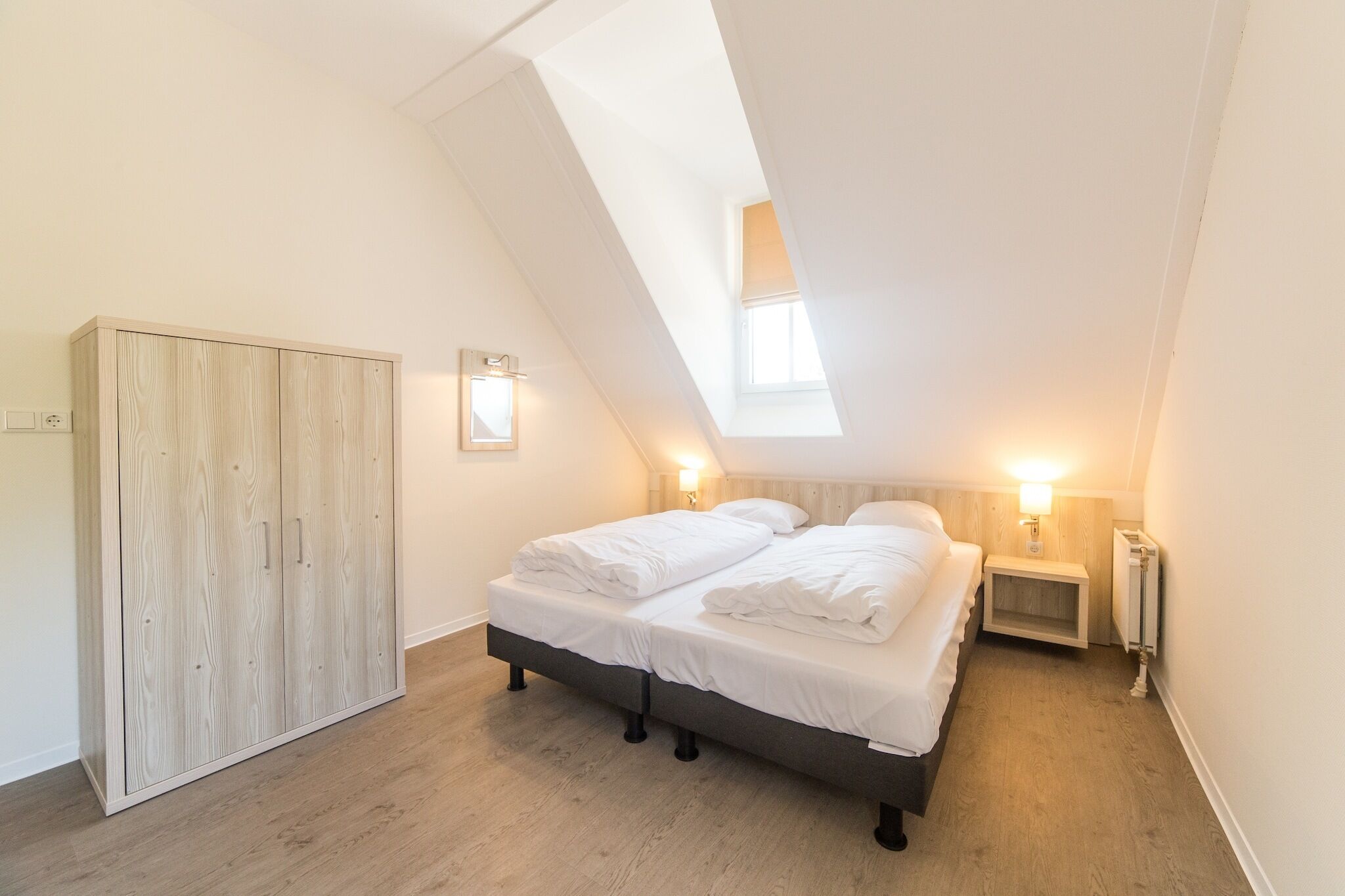 Une chambre avec un plafond de style industriel, un lit avec du linge de lit blanc, une armoire en bois et des lampes de chevet.