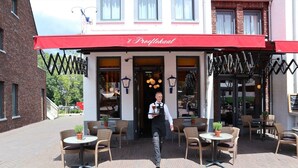 A restaurant with outdoor seating, a red awning, and a waiter carrying a tray. - Sauna, Garden & Indoor Pool (Maastricht)