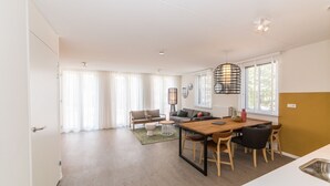 A modern living room with a sofa, a coffee table, and a dining area with a wooden table and chairs. - Sauna, Garden & Indoor Pool (Maastricht)
