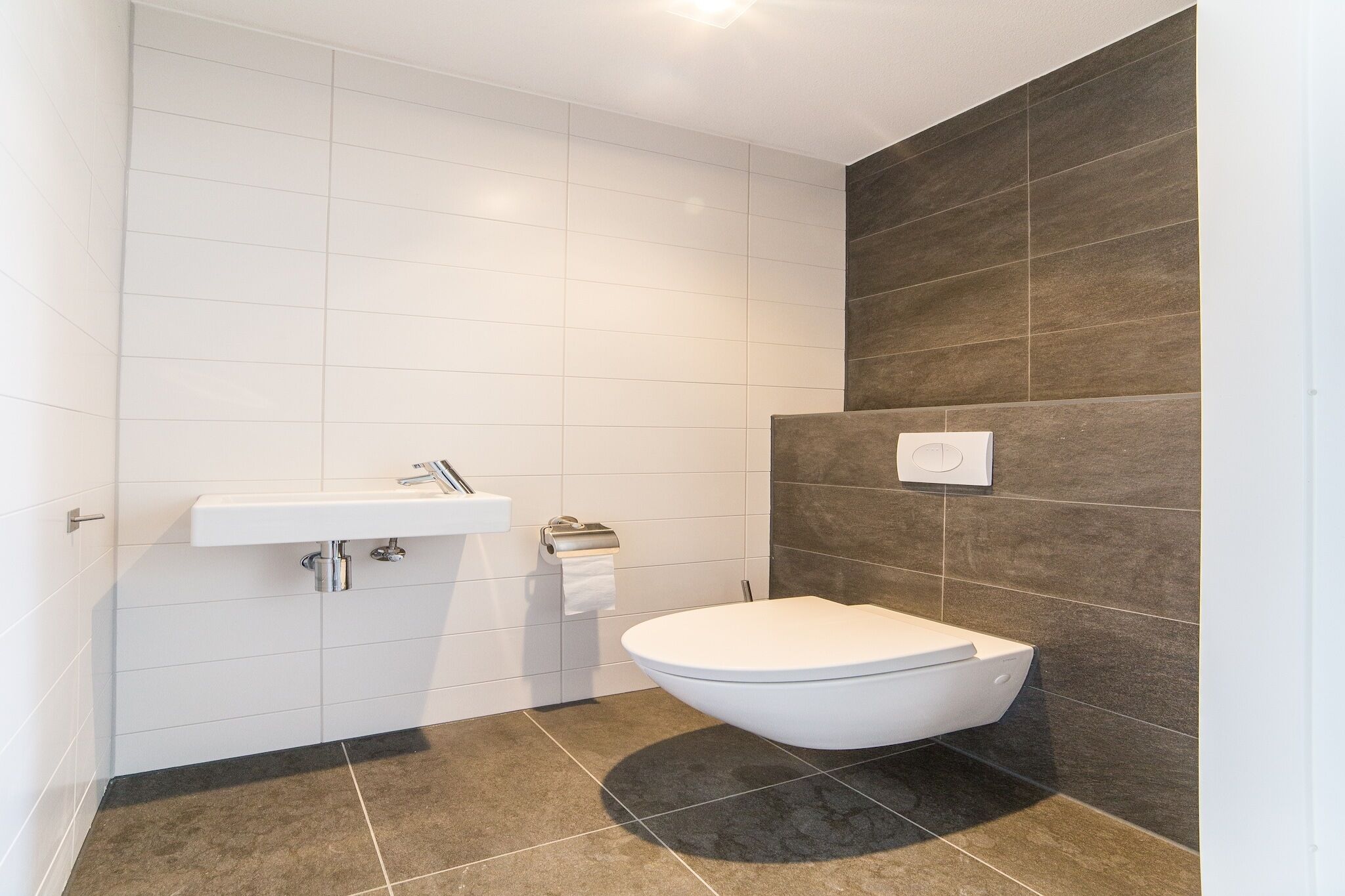 Un baño moderno con un lavamanos blanco, un inodoro y un aplique de pared.