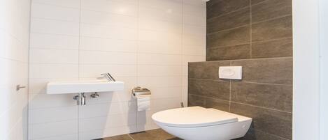 A modern bathroom with a white sink, a toilet, and a wall-mounted light fixture.