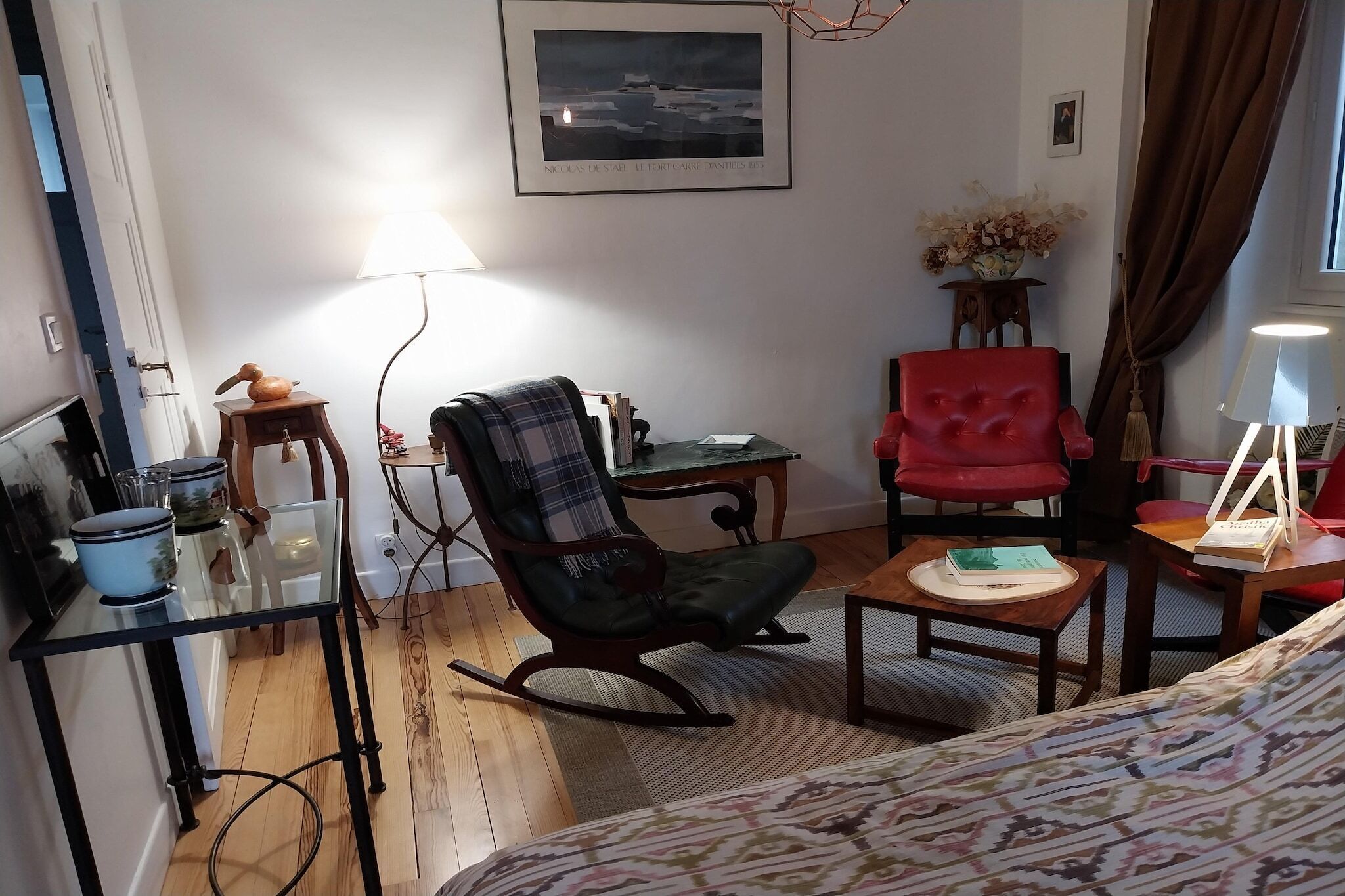 Een gezellige woonkamer met een schommelstoel, een rode fauteuil, een glazen salontafel en een klein bijzettafeltje.