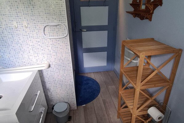 Un baño con pared de azulejos, una puerta azul, un estante de madera y un lavabo blanco.