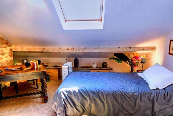 Un dormitorio con cama, escritorio, radiador, ventana y una planta.