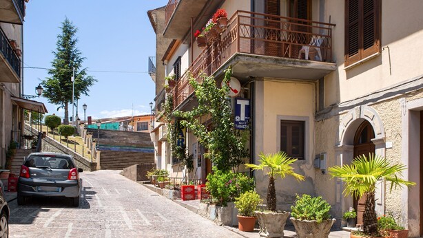 Una calle adoquinada bordeada de edificios, algunos con balcones y macetas.