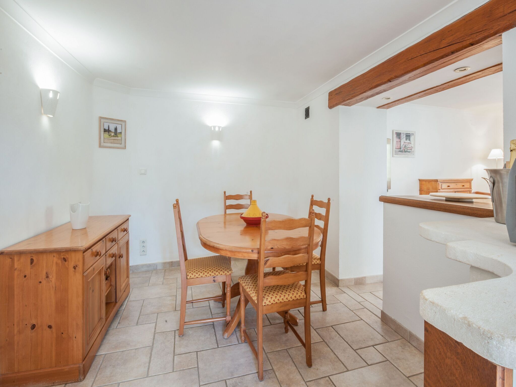 A dining area with a wooden table and chairs, a small cabinet, and a counter with a pitcher.