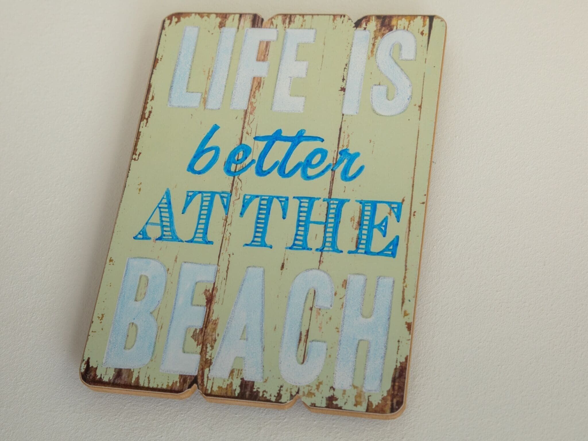 Een verweerd bord met de tekst 'LIFE IS better at the beach' in blauwe en witte letters.