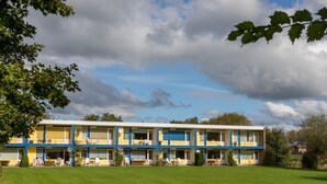 A two-story motel with a flat roof, multiple balconies, and a large lawn area in front.