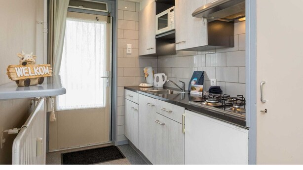 A compact kitchen with white cabinets, a microwave, a kettle, and a gas stove.