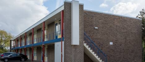 A multi-story building with a brick facade, a staircase, and a parking lot with cars.