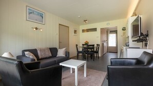 A living room with a sofa, coffee table, and chairs, a dining area with a table and chairs, and a kitchen area with a refrigerator and microwave.