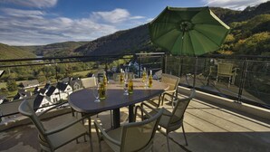 A balcony with a table set for dining, surrounded by wicker chairs, and a green umbrella providing shade. - Modern Penthouse with Sauna (Heimbach)