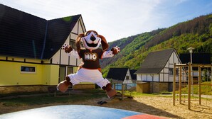 A mascot in a brown and white outfit jumping on a colorful play structure. - Modern Penthouse with Sauna (Heimbach)
