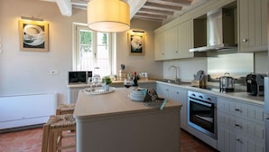 A modern kitchen with a central island, white cabinetry, and a hanging light fixture.