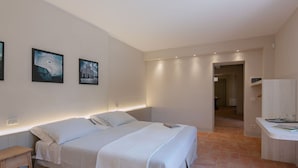A bedroom with a bed, bedside tables, and a desk. There are two wall-mounted lights above the bed and a door leading to another room.