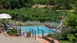 A rectangular swimming pool surrounded by a gravel patio, with a seating area and umbrellas.