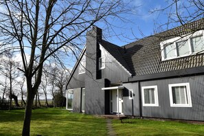 Ein modernes, zweistöckiges Haus mit dunkler Fassade, einem sichtbaren Schornstein und einer Haustür mit einer kleinen Veranda.