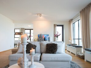 Een moderne woonkamer met een witte bank, een tafel met kaarsen en een televisie op de achtergrond.