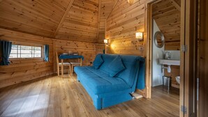 A cozy cabin interior with a wooden floor, a blue sofa, a dining table, and a bathroom with a sink and mirror.