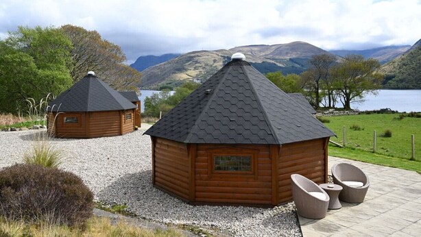 Two wooden cabins with hexagonal roofs, surrounded by gravel paths and greenery, overlooking a lake and mountains. - Leven View Lodges near Glencoe No2 Callart (Fort William)