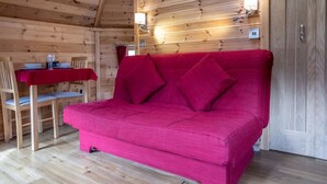 A red sofa in a wooden cabin with a dining table and chairs. - Leven View Lodges near Glencoe No2 Callart (Fort William)