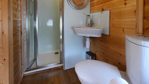 A compact wooden cabin bathroom with a glass-enclosed shower, a white sink, and a toilet. - Leven View Lodges near Glencoe No2 Callart (Fort William)
