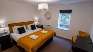 A bedroom with a bed, two bedside tables, a desk, a chair, a window, and a radiator.