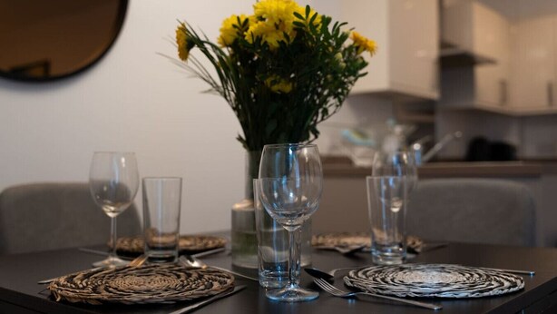 A dining table set with clear glassware, a vase with yellow flowers, and woven placemats.