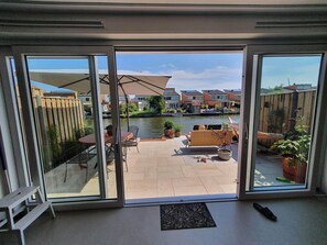 Une porte-fenêtre coulissante donne sur un patio aménagé avec du mobilier d’extérieur, une petite table et des plantes en pot.