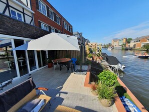 A riverside patio with outdoor furniture, a grill, and a view of the water.