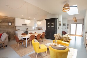 Un salon moderne avec un coin repas, doté d’une grande fenêtre, d’une cheminée et d’une cuisine en arrière-plan.