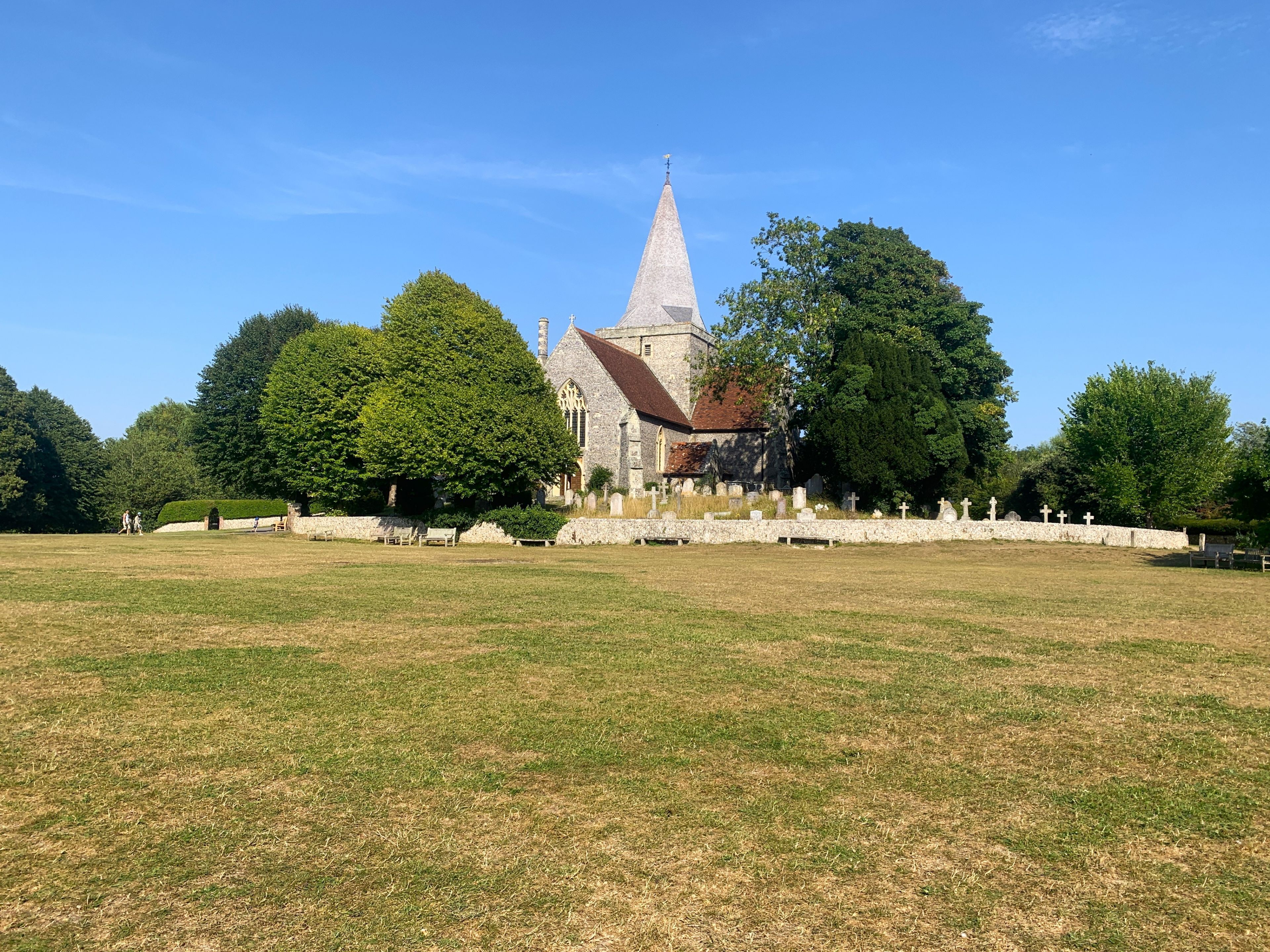 Een kerk met een hoge spits, omringd door een kerkhof met grafstenen en een grasveld.