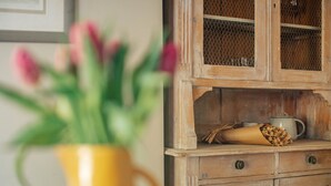 Een houten kastje met een gaasdeur, een gele vaas met bloemen, en een jutssak op de plank.