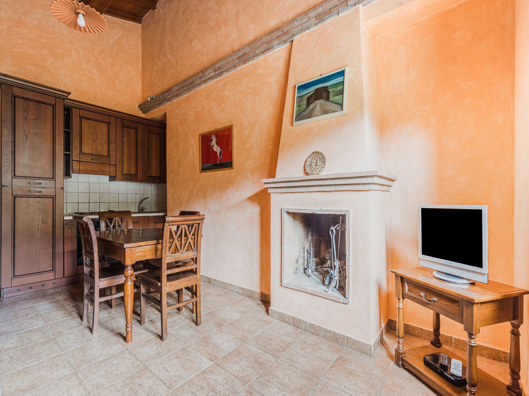 A kitchen with wooden cabinets, a dining table with chairs, a fireplace, and a television on a wooden stand.