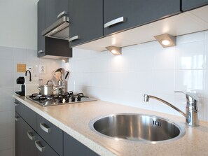 Een moderne keuken met grijze kastjes, een RVS spoelbak en een gasfornuis.