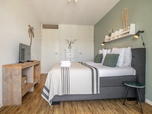 Een slaapkamer met een bed, nachtkastje, lamp en een bureau met een computer.