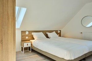 A bedroom with a sloped ceiling, a skylight, a round mirror, a bedside table with a drawer, and a bed with white bedding.