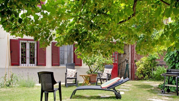 Een terras met buitenmeubilair, waaronder stoelen en een loungestoel, onder een boom.
