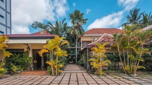 A courtyard with a tiled walkway, palm trees, and buildings with red-tiled roofs. - Marirath Boutique Hotel  (Siem Reap)