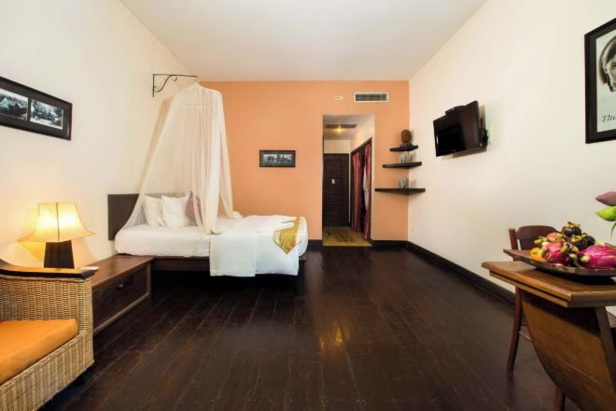 Een hotelkamer met een bed, nachtkastje, stoel, tafel met fruit en een televisie.
