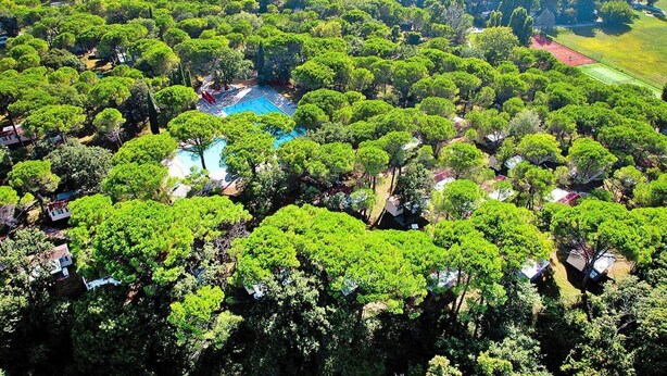 Luchtbeeld van een resort met een centraal zwembad, omringd door weelderige begroeiing en verschillende tennisbanen.