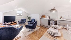 A modern living room with a flat-screen TV, dark leather chairs, a dining table set for four, and a kitchen with white cabinets and a sink. - Central Cosy Harrogate Apartment (North Yorkshire)