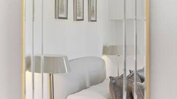 Um quarto com uma cama branca, duas luminárias de cabeceira, uma mesa de cabeceira com gaveta e três quadros na parede.