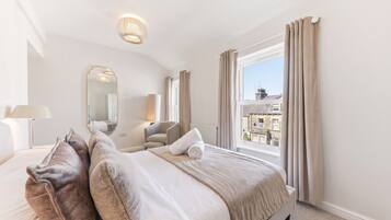 A hotel room with a large bed, a chair, a desk, a mirror, and a window with curtains.