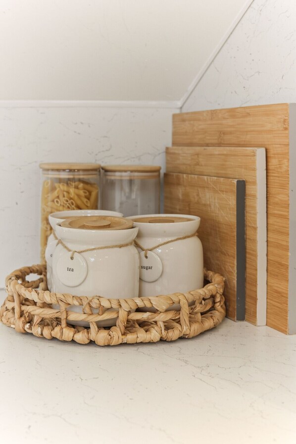 A kitchen area with a woven basket containing jars labeled 'tea' and 'sugar,' and a wooden cutting board.