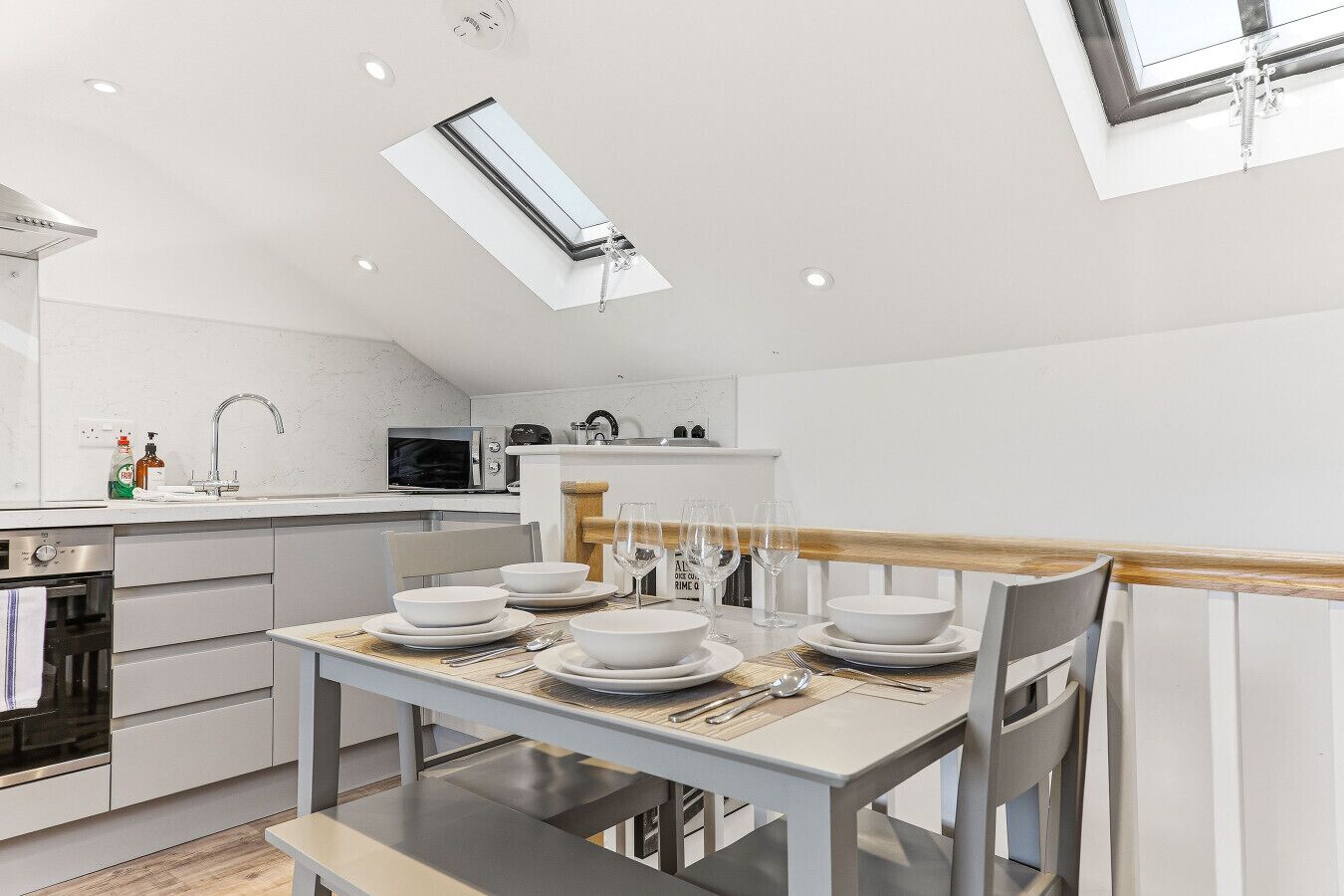 A modern kitchen with a skylight, white cabinetry, a dining table set with plates and glasses, and a microwave.