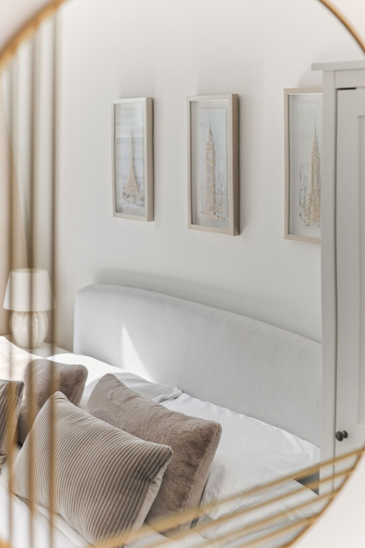 A bedroom with a white headboard, two framed pictures on the wall, and a bed with multiple pillows.